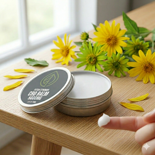 An opened tin of extra strength 5000mg CBD balm showing a smooth white texture next to yellow arnica flowers on a wooden table, showcasing natural joint recovery ingredients.